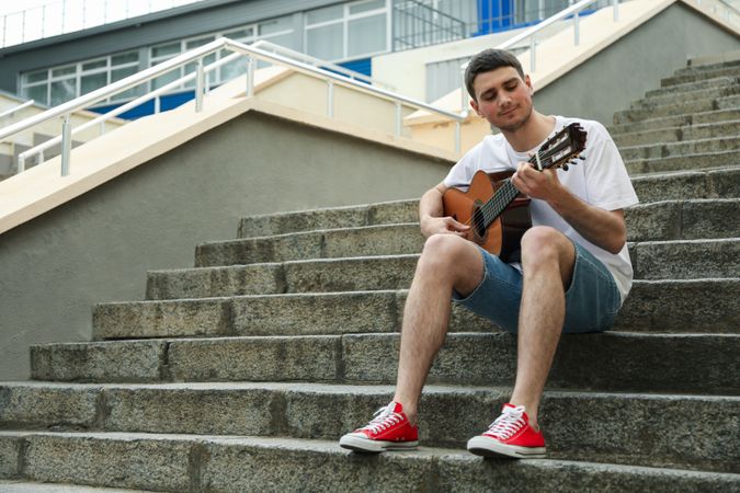 Young man sits on the steps and play on guitar