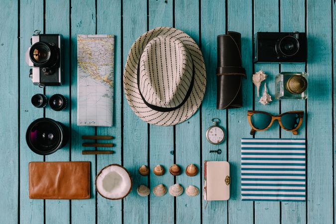 Mix of travel items; hat, camera, map, compass, seashells, arranged on blue background