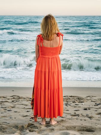 Woman in red dress looking along at seaside