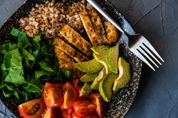 Top view of healthy fresh meal with avocado, grains, tomatoes & spinach