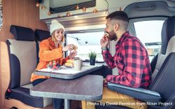 Male and female friend enjoying breakfast rolls and coffee in back of van 48Yvqb