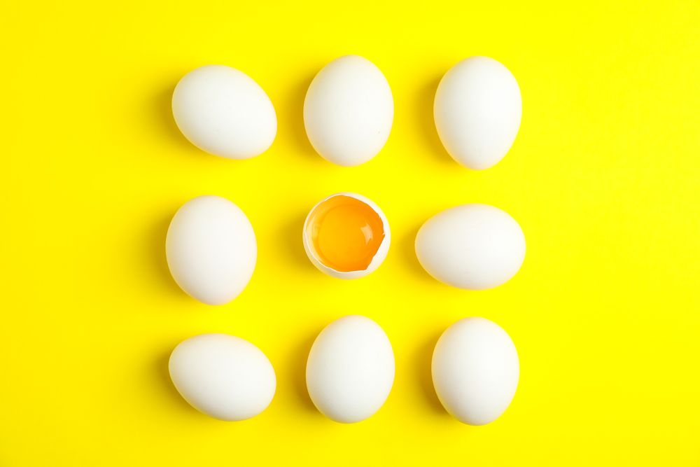 Flat lay composition with chicken eggs and half with yolk on color background, space for text