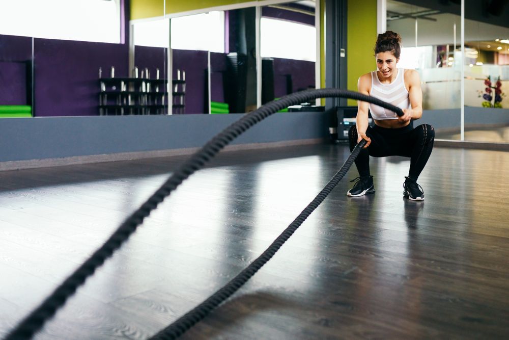 Woman working out upper body with ropes in gym while squatting
