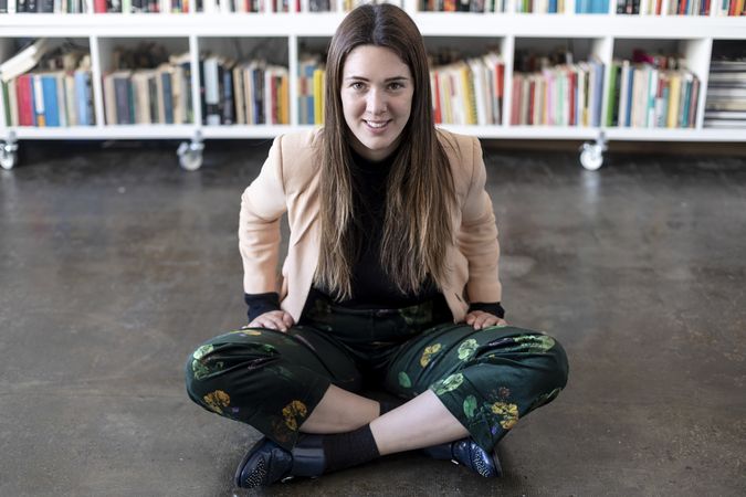 Portrait of a happy woman sitting cross legged in front of book shelf