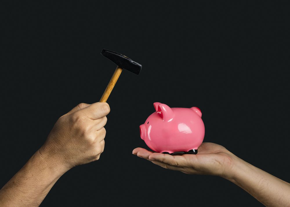 Hand holding hammer over pink piggy bank on dark background