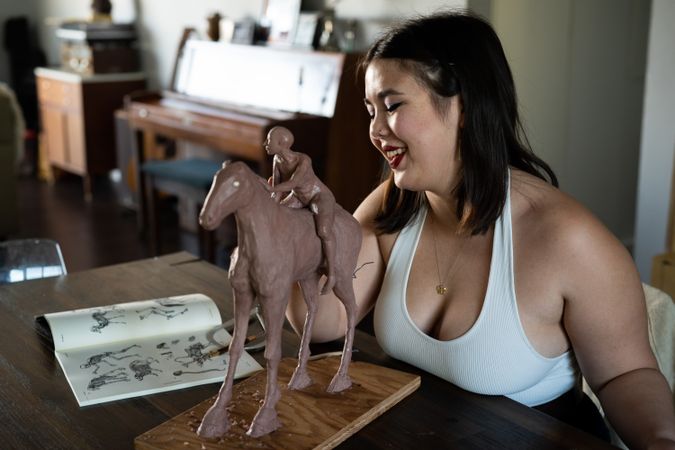 Woman in tank top smiling while sculpting horse and rider