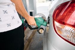 Close-up Detail of the arms and hands of a young brunette woman refueling herself at a small gas station.