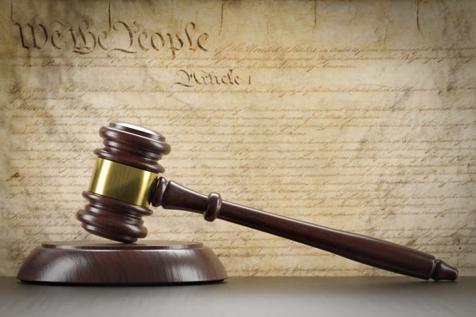 United States Constitution On Wall with Gavel Resting on Table in Front.