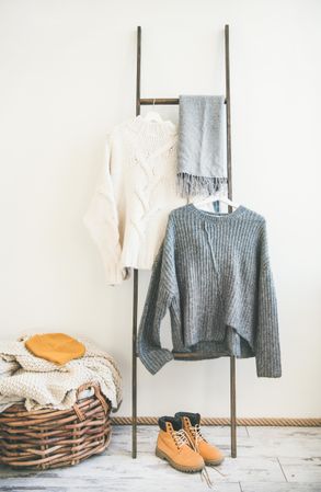 Woolen sweaters, grey scarf, winter boots on modern garment rack, with thatched basket, close up