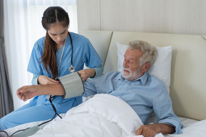 Asian nurse caregiver checking blood pressure of male patient