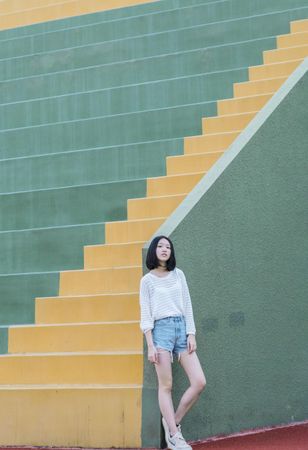 Woman in light shirt and blue denim shorts standing beside staircase