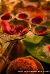 Rose petals on golden panch aarti beside green leaves on a table 0yGdW4