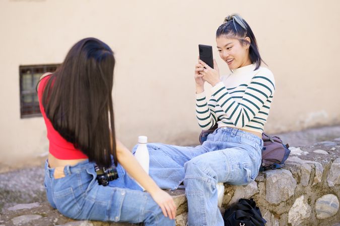 Woman taking her friends picture as they sit outside