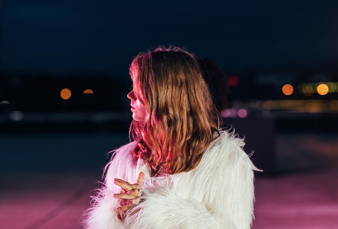 Woman looking to the side in shaggy faux fur in moody red light at night