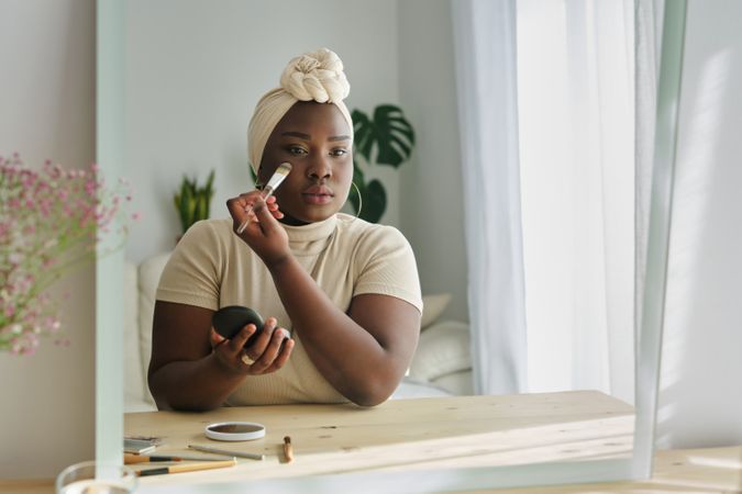 Black woman applying cosmetic on face with brush
