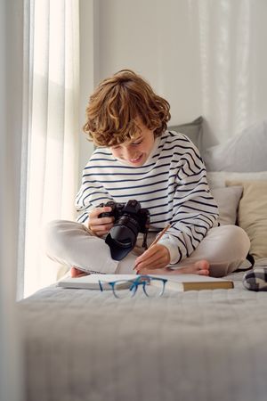 Smiling schoolboy with photo camera on bed at home