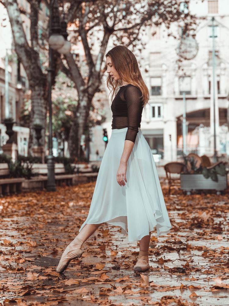 Young ballerina stretching toe in autumn park