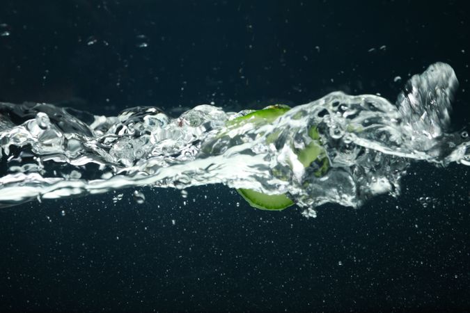 Side view of water splashing on dark background with cucumber