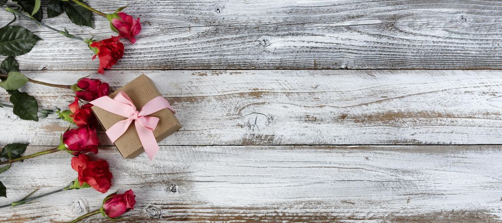 Circle of real red flowers plus giftbox on rustic wooden planks