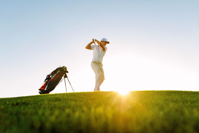 Golf player swinging golf club on sunny day