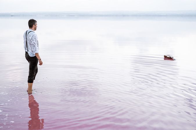 Man in wet shirt picking up guitar floating in water