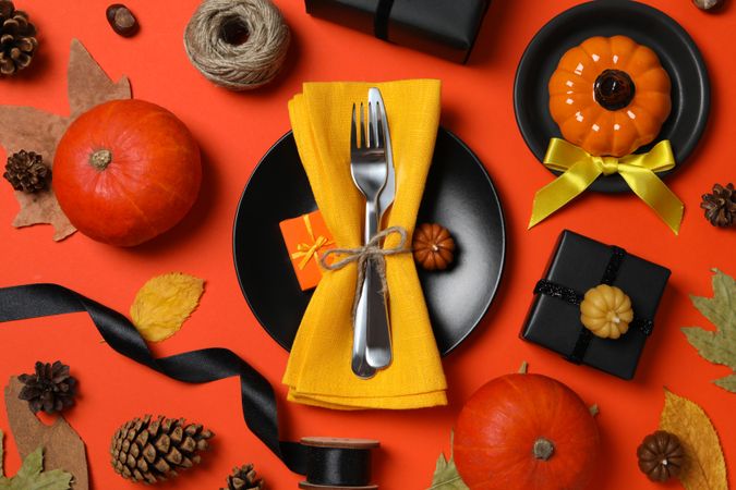 Cutlery on plate, pumpkins and leaves on red background, top view