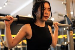 Young Asian Woman in Athletic Wear is Performing Squats on the Smith Machine at the Gym