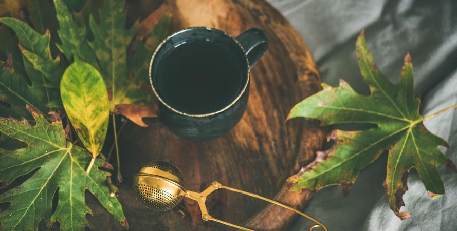 Fall leaves next to tea cup and infuser on wooden tray