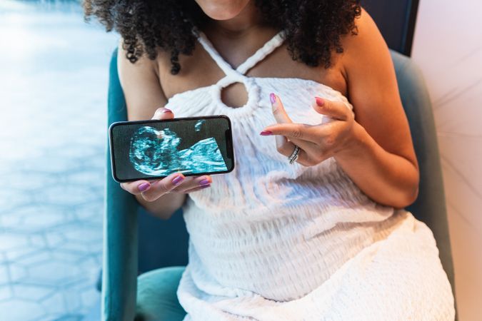 Anonymous Black pregnant woman showing baby ultrasound picture to laptop