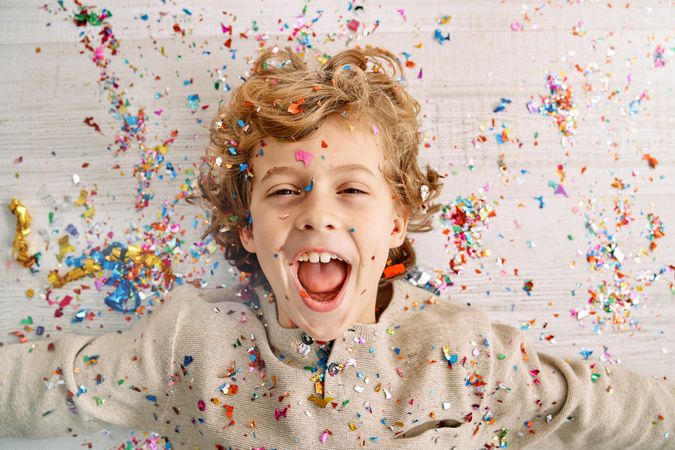Excited little boy screaming joyfully covered with confetti