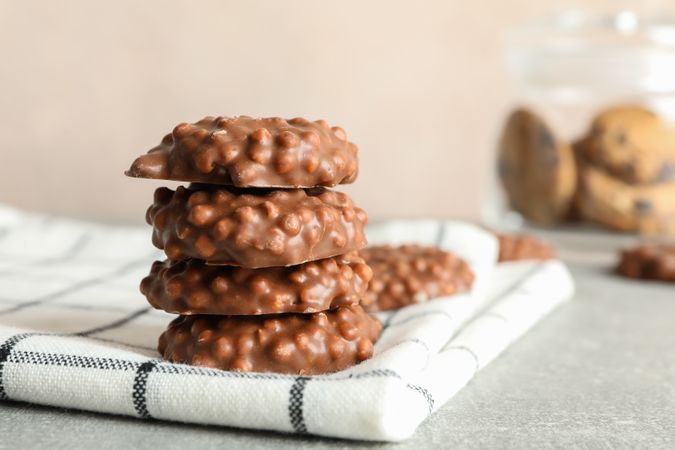 Stack of chocolate cookies on kitchen towel against light background, space for text