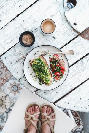 Avocado toast on sourdough bread, cherry tomatoes, coffee, with feet, on light background