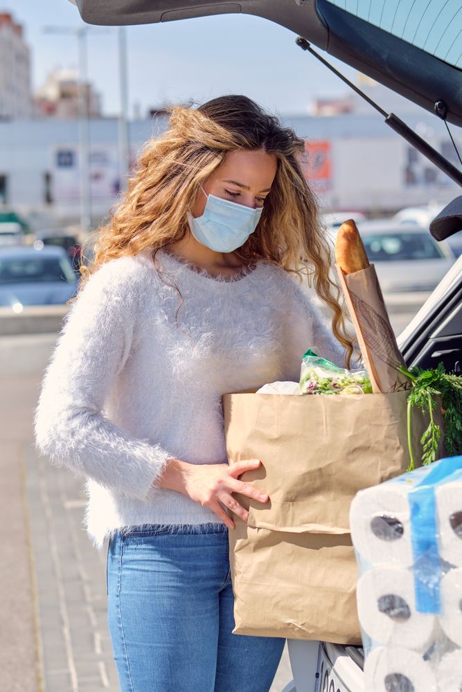 Woman in mask putting grocery bags in car trunk