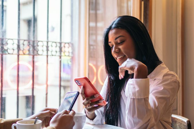 Black Latina woman sitting in coffee shop using smartphone.