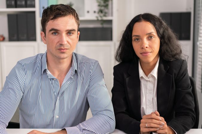 White man and Latina colleague sitting behind desk in workplace