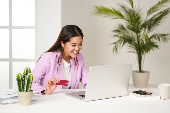 a smiling young Asian woman excited about online shopping from the office