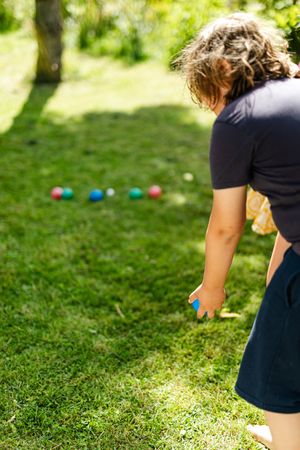 Back view of a person throwing a blue ball standing on green grass