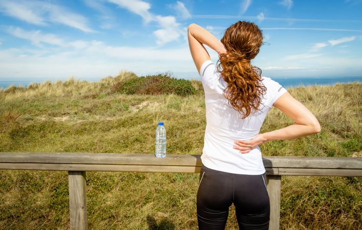 Woman in athletic gear holding hurt upper shoulders overlooking coast