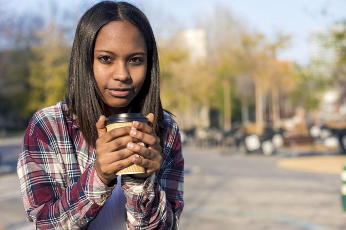 Female in plaid shirt holding a to go coffee