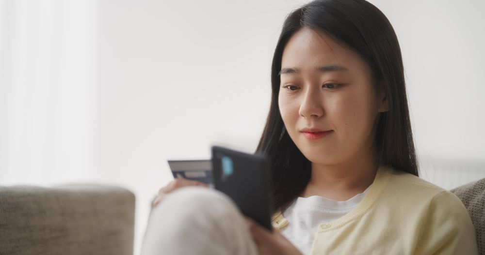 Asian Woman Doing Mobile Retail Therapy, Browsing Online Shopping Website in a Living Room