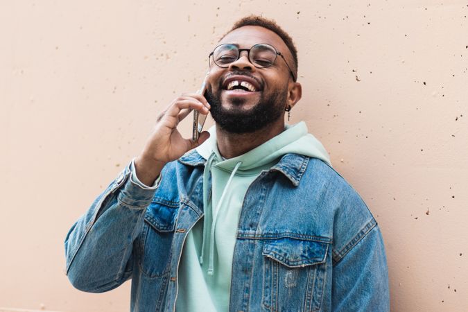 Cheerful Black man talking on phone near wall