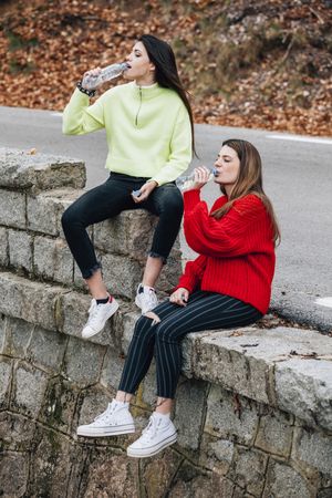 Women in sweaters drinking from bottles near road