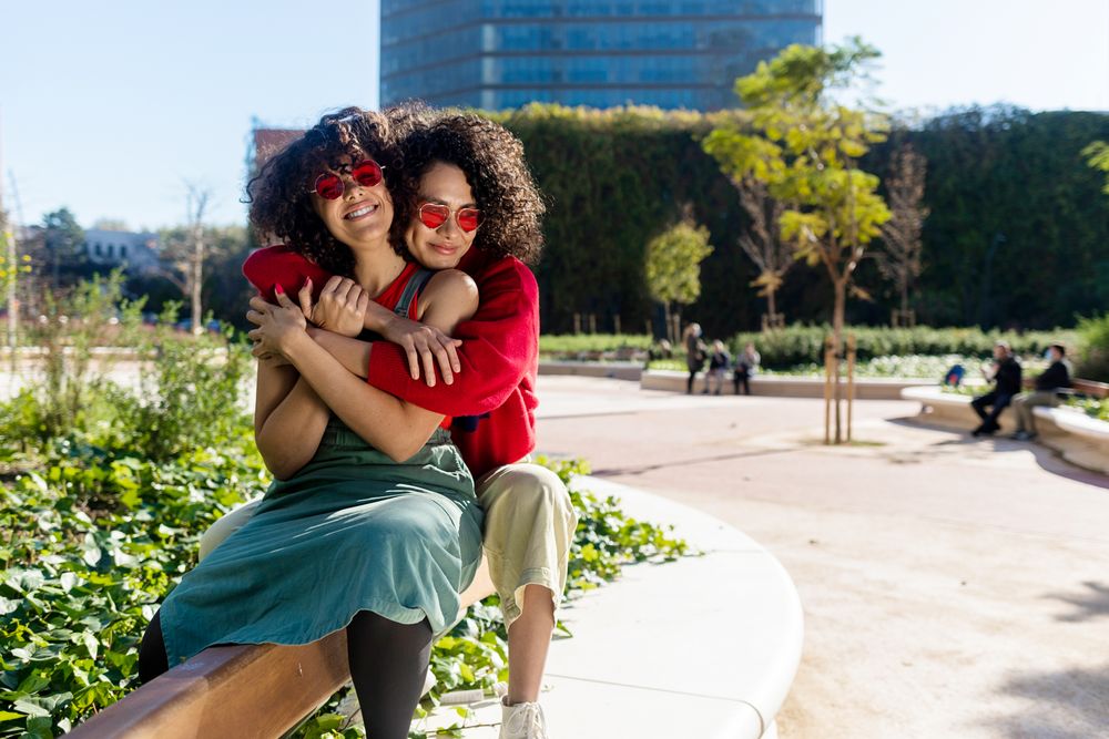 Two female friends sitting and smiling together in city park together