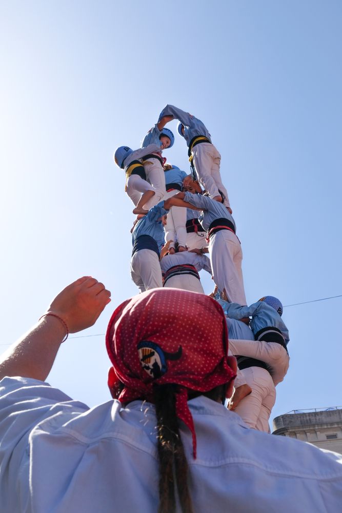 Person looking at and raising hand toward boys in uniforms standing on top of each other outdoor