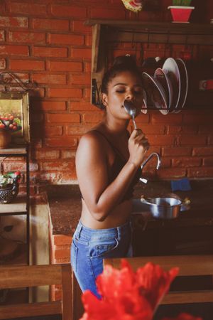 Woman in dark bra and denim pants eating with spoon in the kitchen