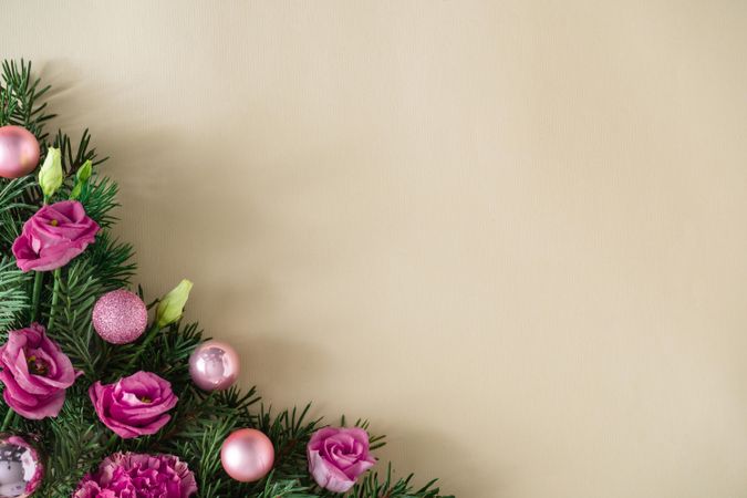 Pine branches, pink flowers, and festive baubles on beige background