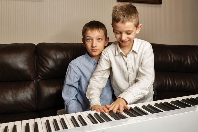 Older boy helping younger boy play the keyboard.
