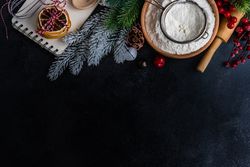 Notebook on kitchen counter surrounded by baking ingredients and Christmas decorations with copy space