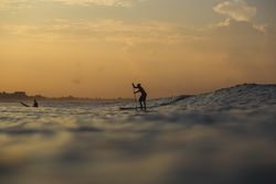 Men with paddle on surf board between waving water at sunset