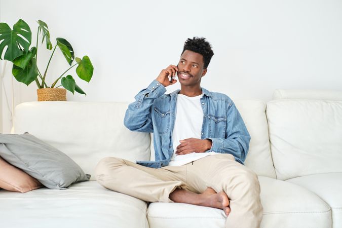 Smiling Black man speaking on smartphone in living room